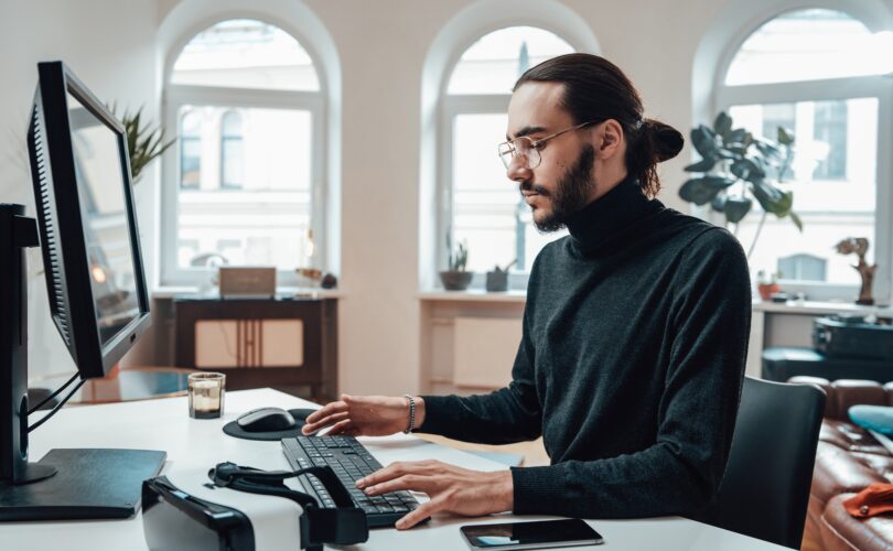 Bearded office worker with long hairs types on keyboard in office