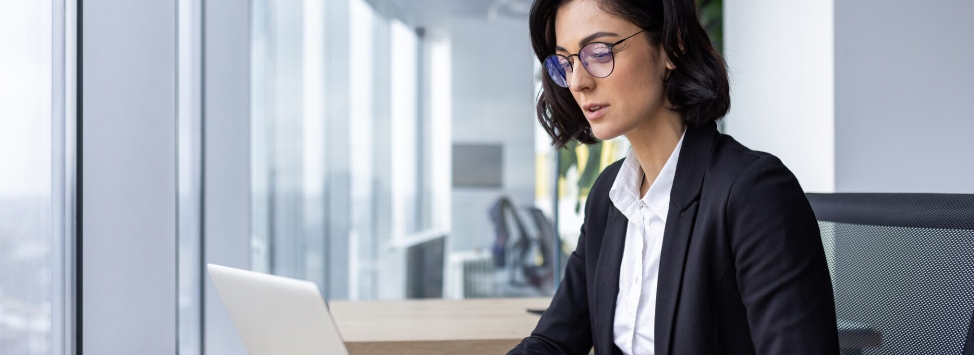 Serious confident thinking businesswoman at work with laptop inside office, female office worker in