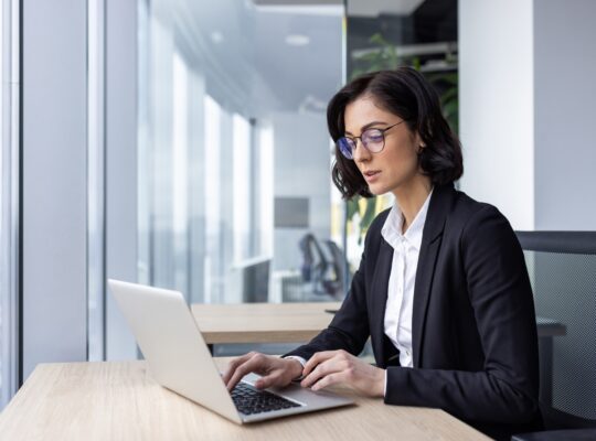 Serious confident thinking businesswoman at work with laptop inside office, female office worker in