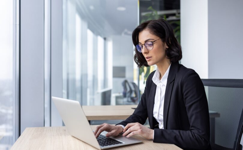 Serious confident thinking businesswoman at work with laptop inside office, female office worker in